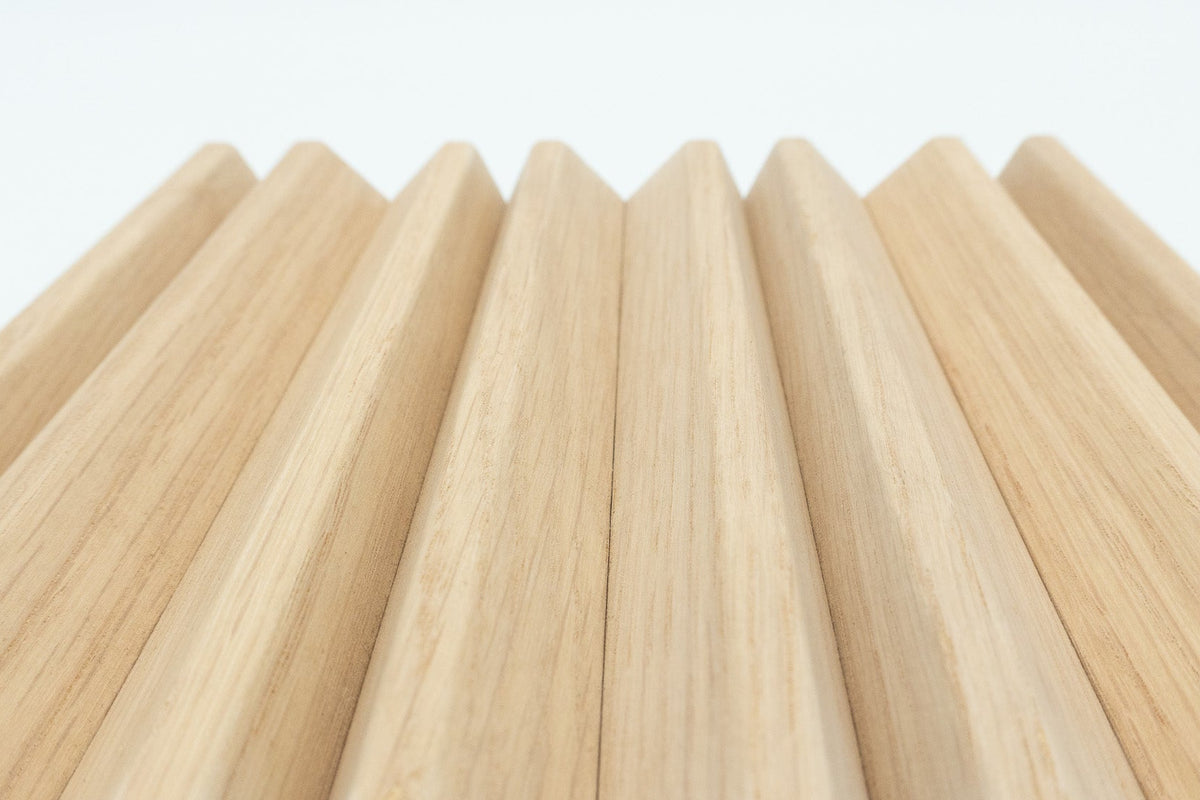 A close-up of a light natural wood panel with a repeating wavy or pleated profile and visible wood grain, photographed against a plain white background.